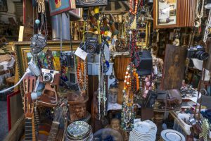 A charming Athens thrift shop with vintage treasures and retro finds spilling onto the cobblestone street, inviting passersby to explore its eclectic collection