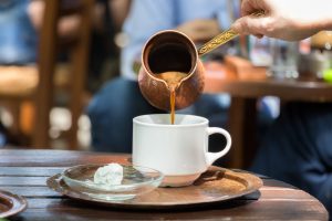 Woman pouring Greek coffee on a white cup.
