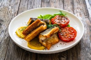 Seared eel steaks and fried tomatoes served on wooden table