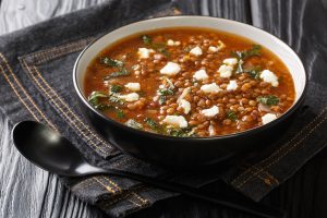 Fakes a traditional Greek vegetarian soup made from brown lentils with tomatoes, oil and feta close-up in a plate on the table. horizontal