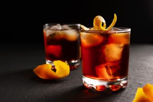 Negroni alcoholic cocktail in two glasses decorated with orange peel with ice cubes on a dark table
