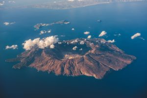 Aerial view of Nisyros island, Greece Aerial view over Nisyros island, Greece. Nisyros is a volcanic Greek island and municipality located in the Aegean Sea. It is part of the Dodecanese group of islands, situated between the islands of Kos and Tilos.
Its shape is approximately round, with a diameter of about 8 km and an area of 41.6 km2. Several other islets are found in the direct vicinity of Nisyros, the largest of which is Gyali, with a population of 22 citizens.
