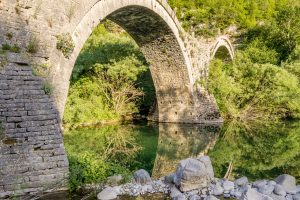 Plakidas arched stone bridge reflected in the water.