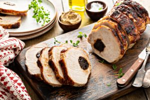 Roasted pork loin stuffed with prunes sliced on wooden board served with grainy mustard, sunday roast recipe